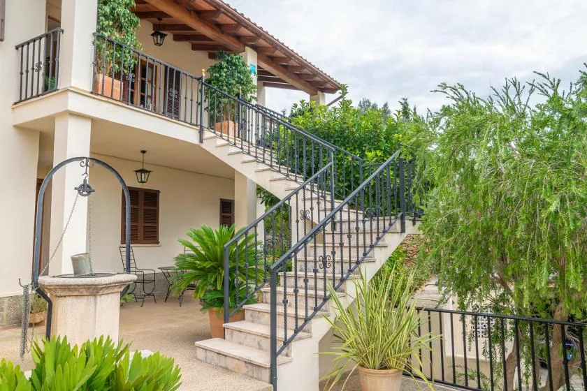 Una escalera exterior con barandillas oscuras sube junto a un patio frondoso.