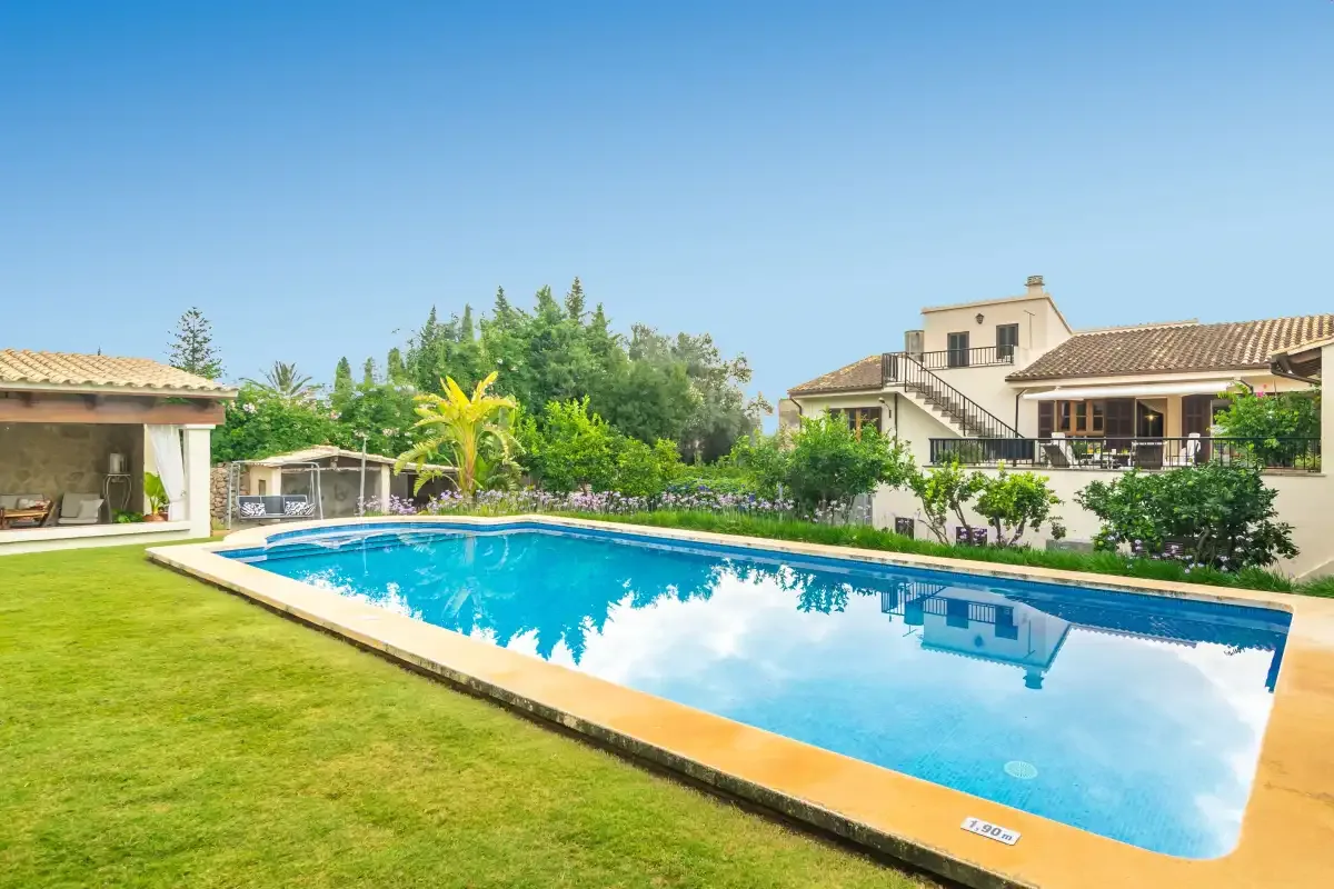 Una piscina está junto a un césped, con una casa al fondo.