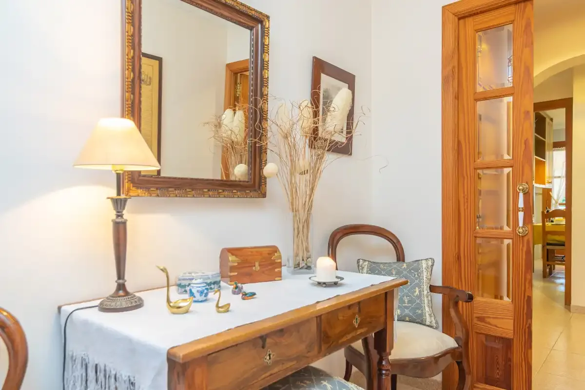 Una habitación amueblada con escritorio de madera, lámpara de mesa y espejo de pared.