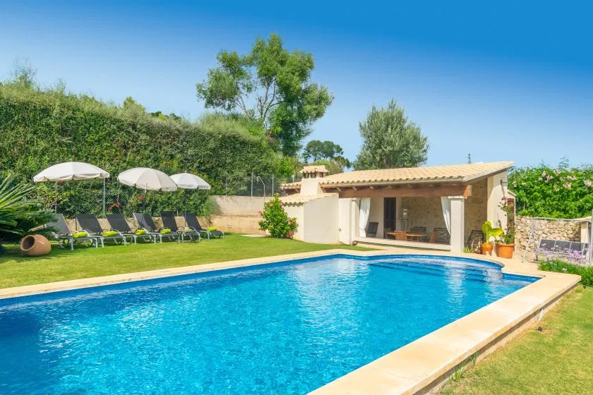 Una piscina al aire libre está junto a una pequeña construcción y un césped.