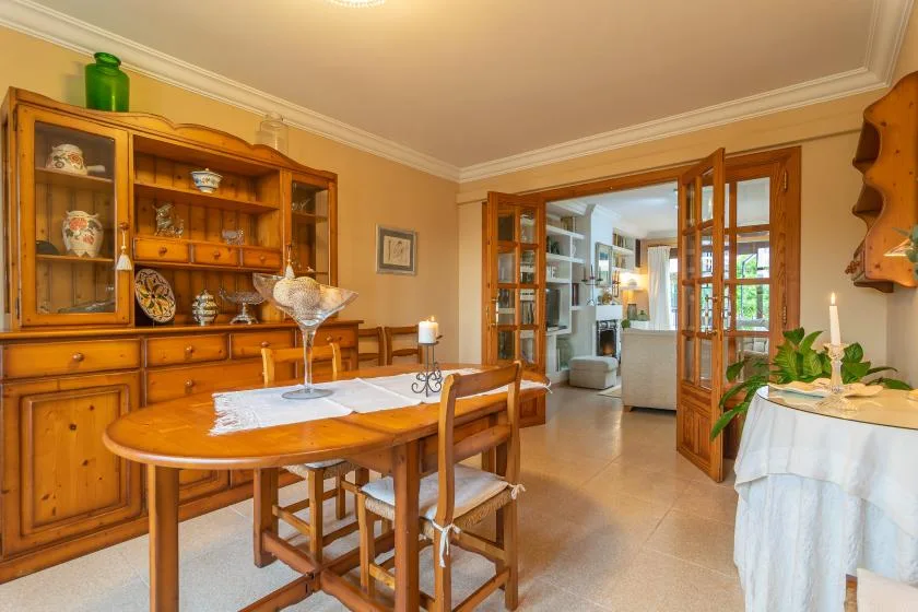 Un comedor con una mesa de madera y puertas de vidrio abiertas hacia una zona de estar.