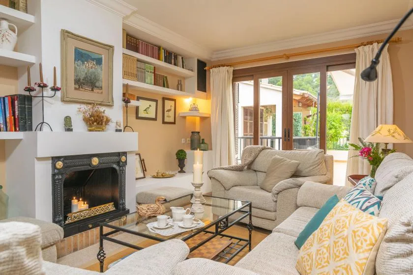 Una sala de estar con asientos, una chimenea y puertas de vidrio hacia un jardín.