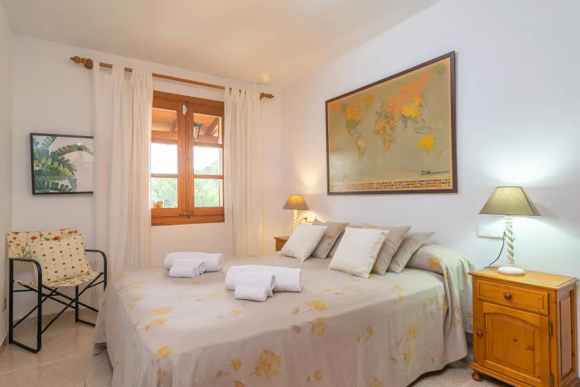 Un dormitorio con una cama bajo un mapa del mundo enmarcado y una ventana.