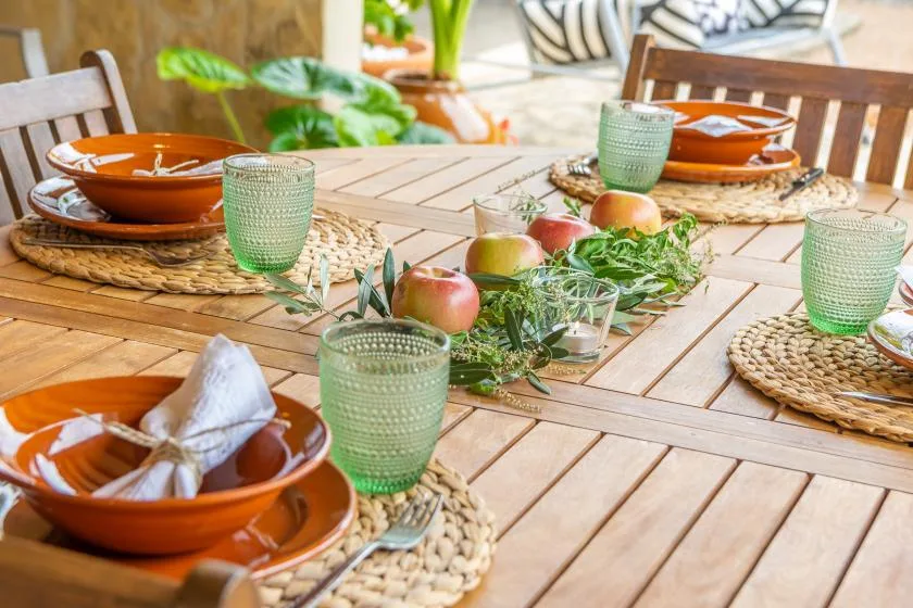 Una mesa de comedor de madera está puesta con platos naranjas, vasos verdes y fruta.