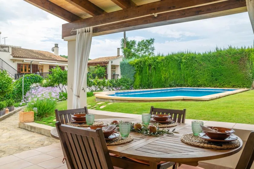 Una zona de comedor en el patio da a una piscina y un césped verde.
