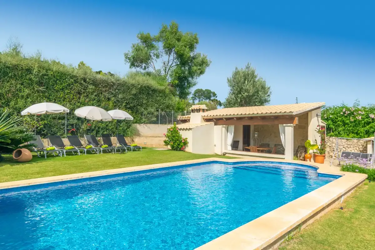 Una piscina junto a un edificio bajo, con asientos y vegetación alrededor.