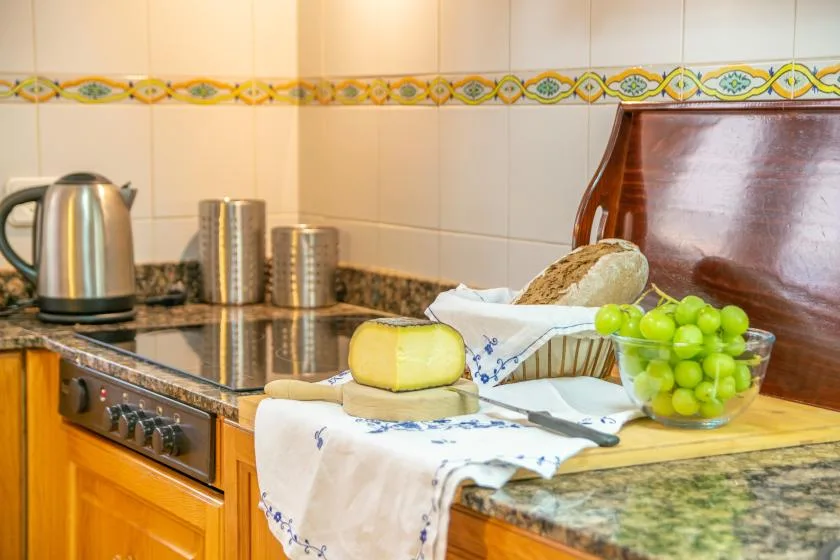 Una encimera de cocina alicatada sostiene una tetera, pan y un cuenco de uvas verdes.
