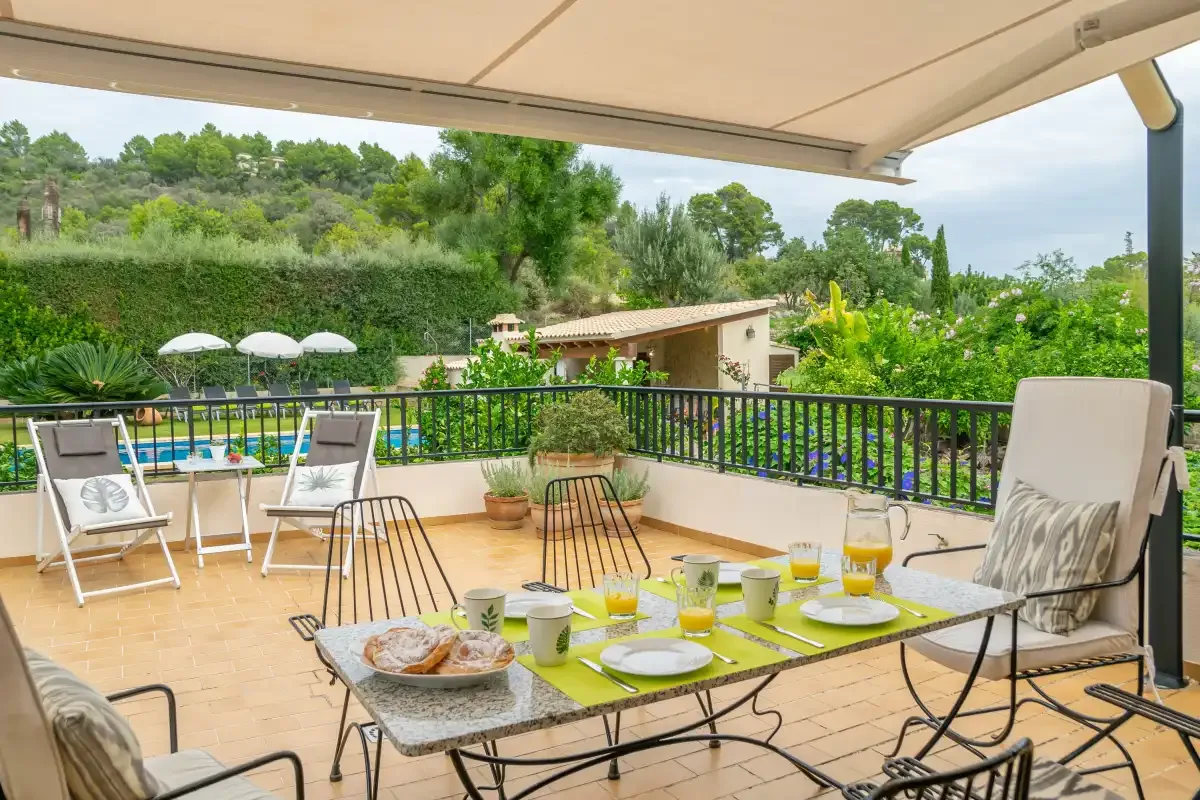 Una terraza cubierta con comedor da a un jardín y una piscina.