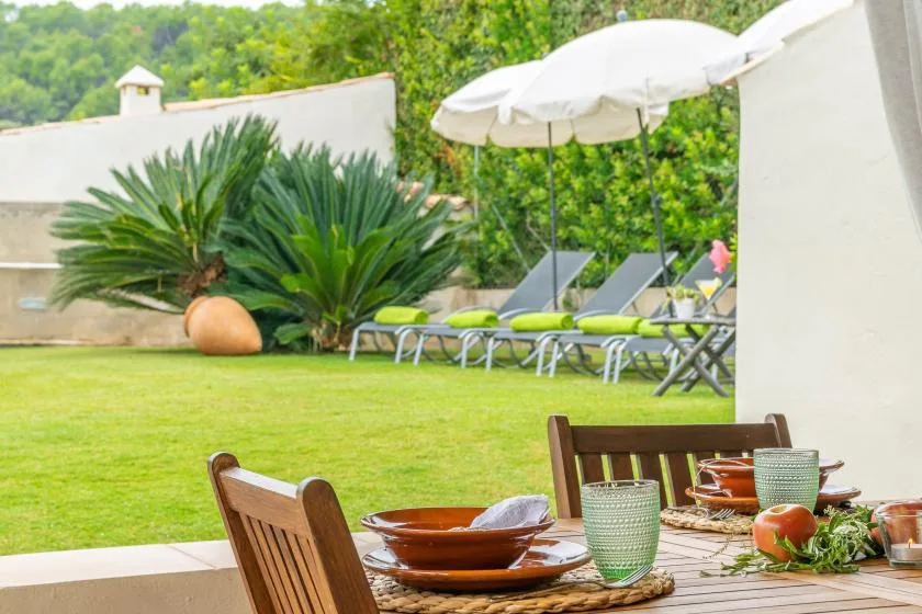 Una zona de comedor en el patio del jardín da a un césped con tumbonas y sombrillas.