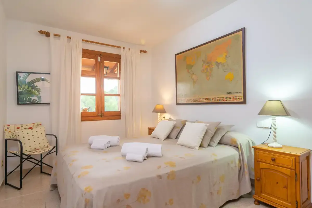 Un dormitorio luminoso con cama doble, mesillas de noche y una ventana.