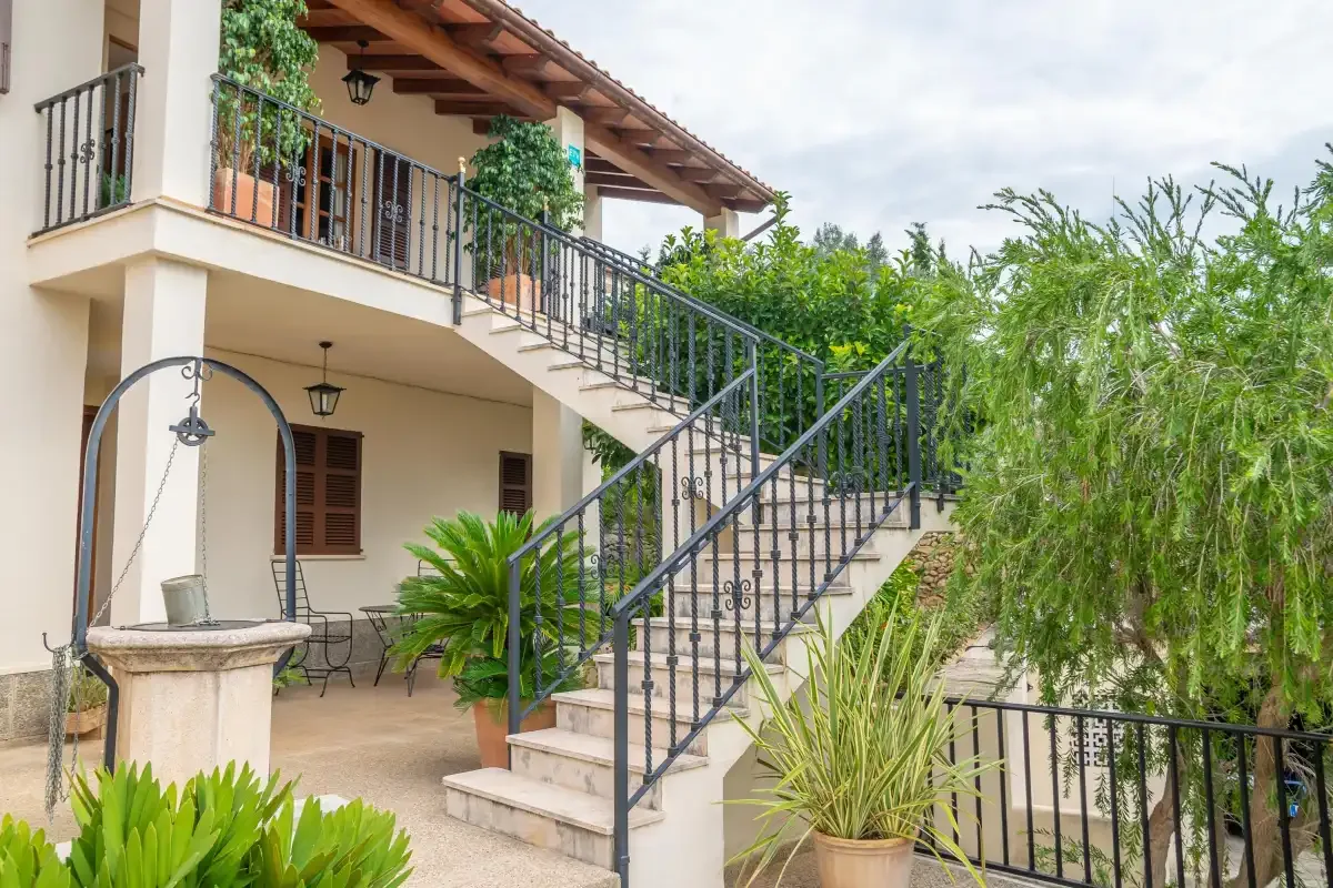 Exterior de una casa con escalera, balcón y jardín frondoso.
