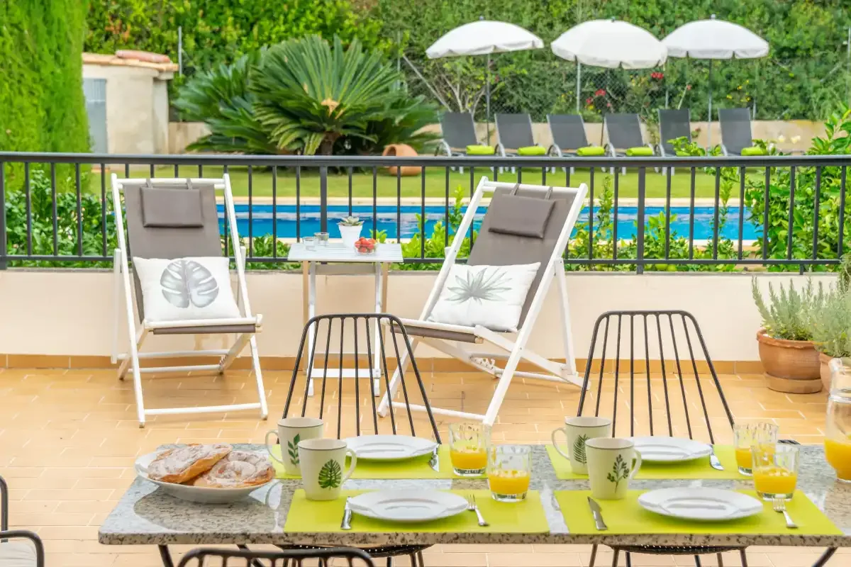 Un comedor en el patio con la mesa puesta, asientos y una piscina al otro lado de la barandilla.