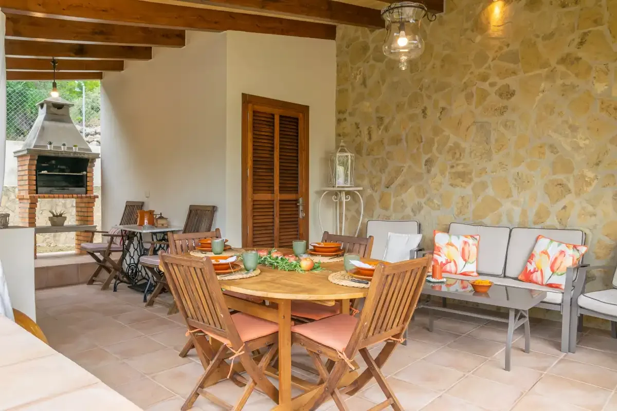 Un comedor en un patio cubierto con una mesa de madera y asientos acolchados.