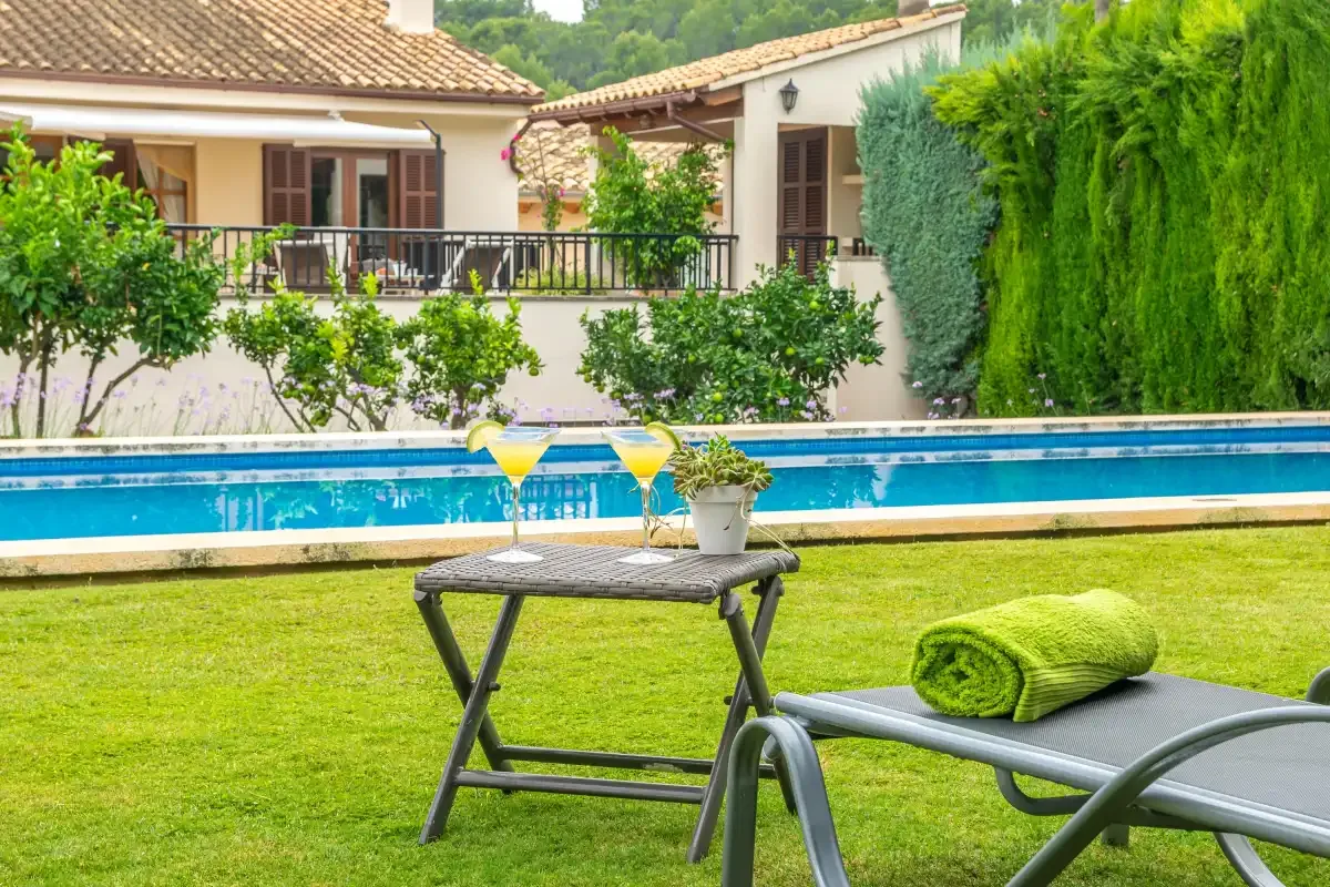 Un jardín junto a la piscina, con asientos y una mesita al lado del agua.