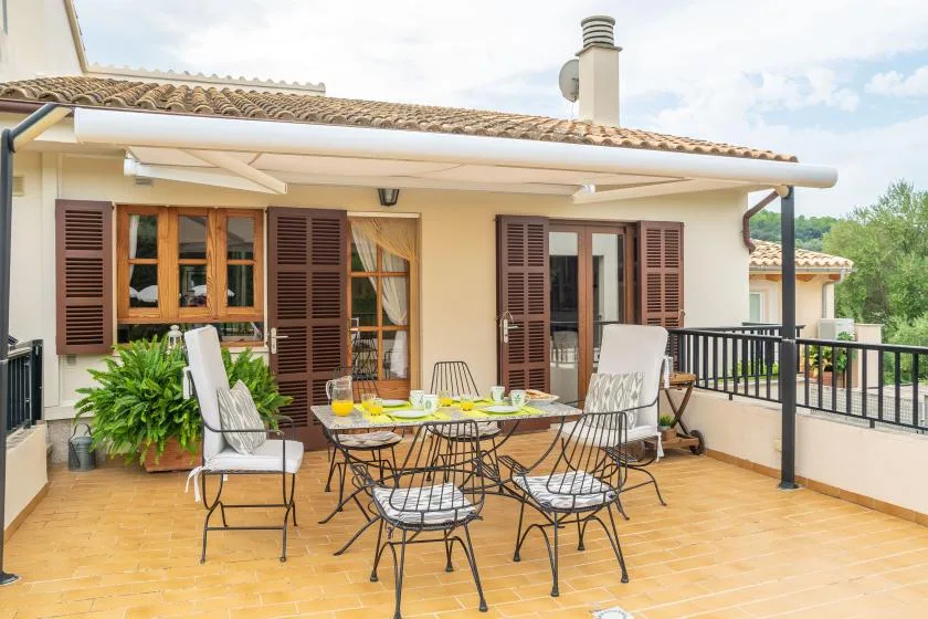 Una terraza de baldosas tiene asientos al aire libre y una mesa junto a la casa.