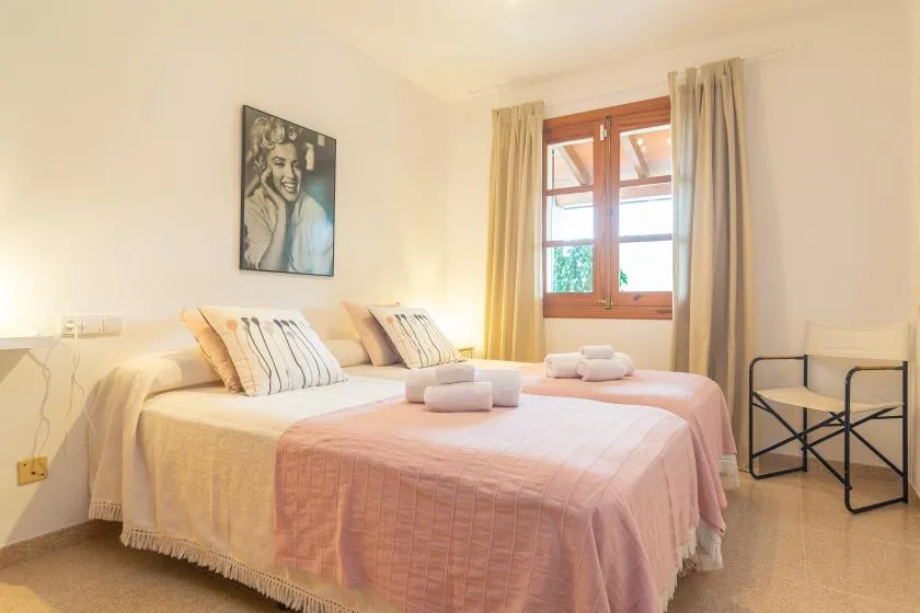 Un dormitorio con dos camas vestidas con ropa de cama rosa claro bajo una ventana.