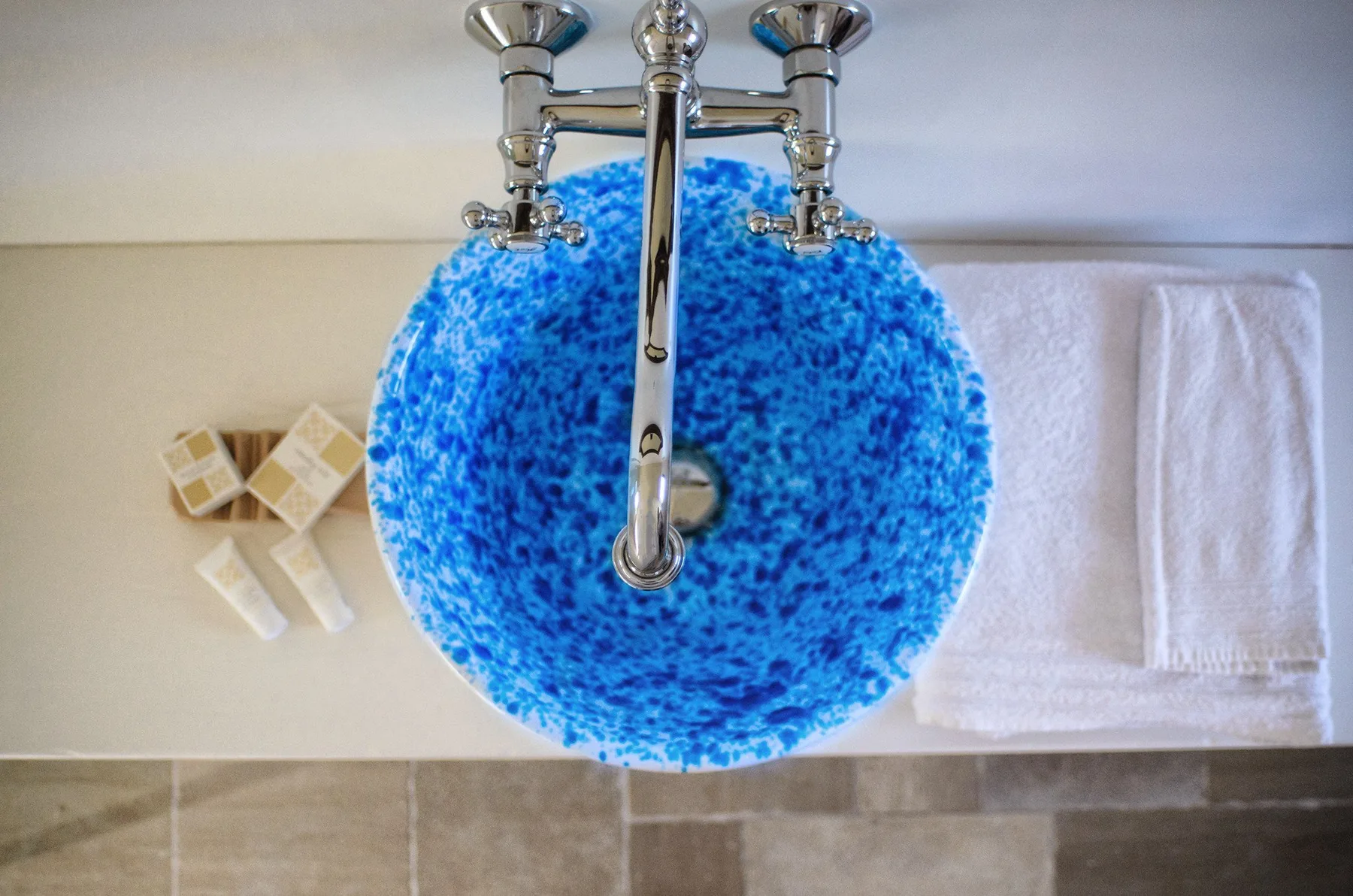Un lavabo azul con grifo cromado, jabón y una toalla doblada sobre la encimera del baño.