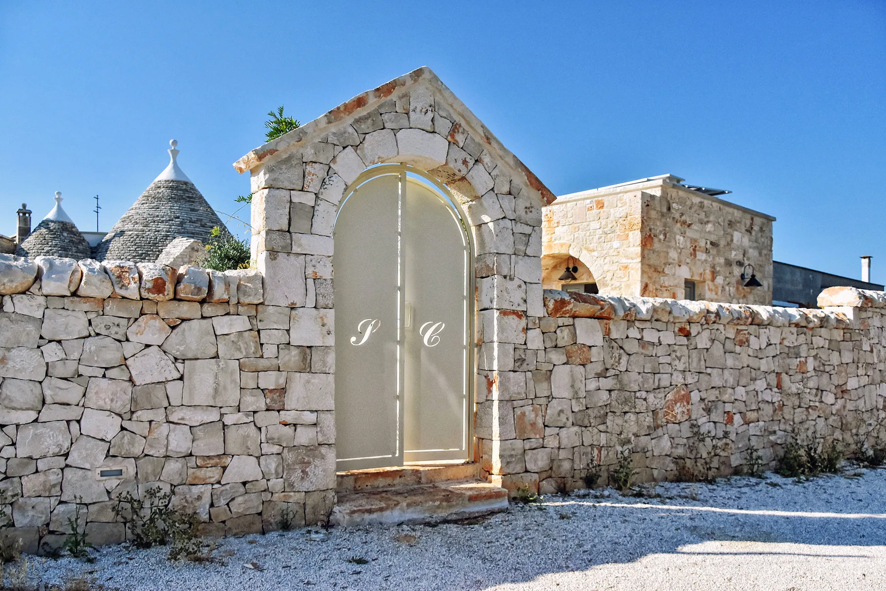 Un muro de piedra con una puerta metálica arqueada bajo un cielo azul despejado.