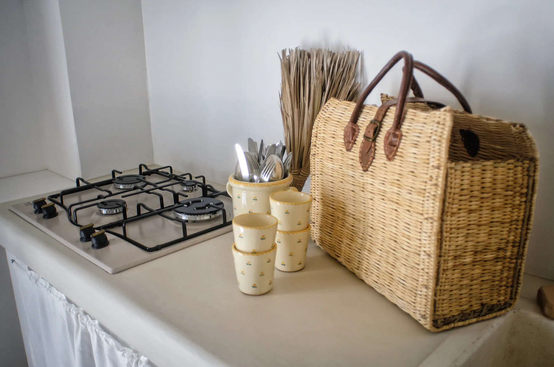 Una encimera de cocina con una estufa de gas, recipientes para utensilios y una cesta tejida.