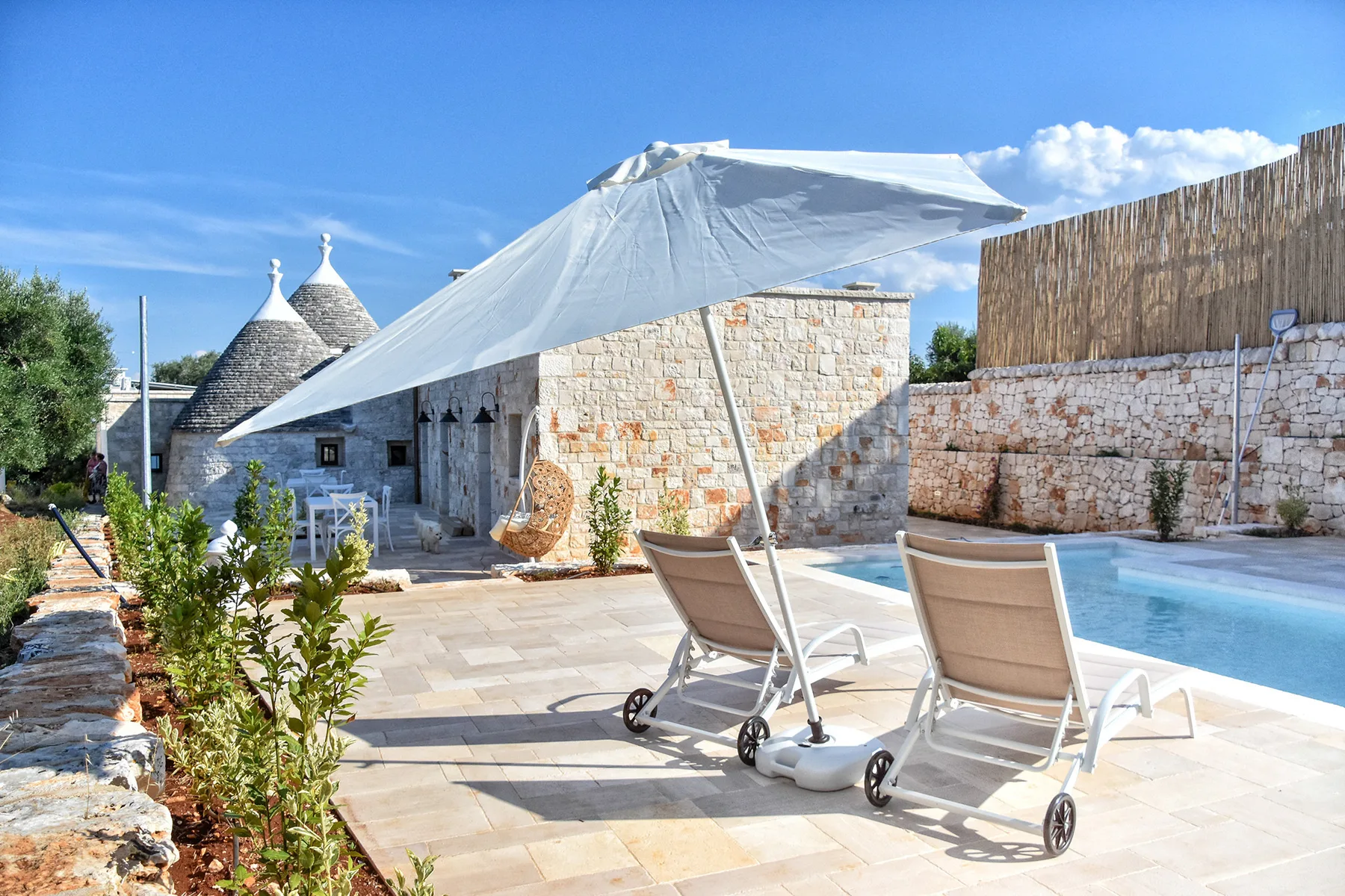 Un patio de piedra con piscina y asientos de descanso a la sombra.