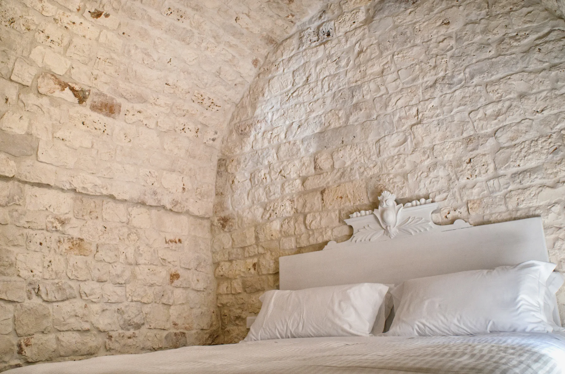 Una cama está junto a paredes de piedra clara en un dormitorio.