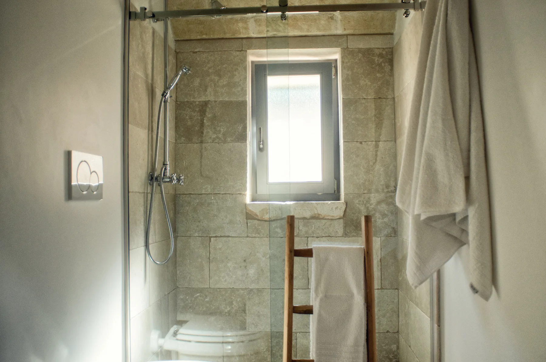 Zona de ducha en un baño con azulejos, una ventana y toallas.