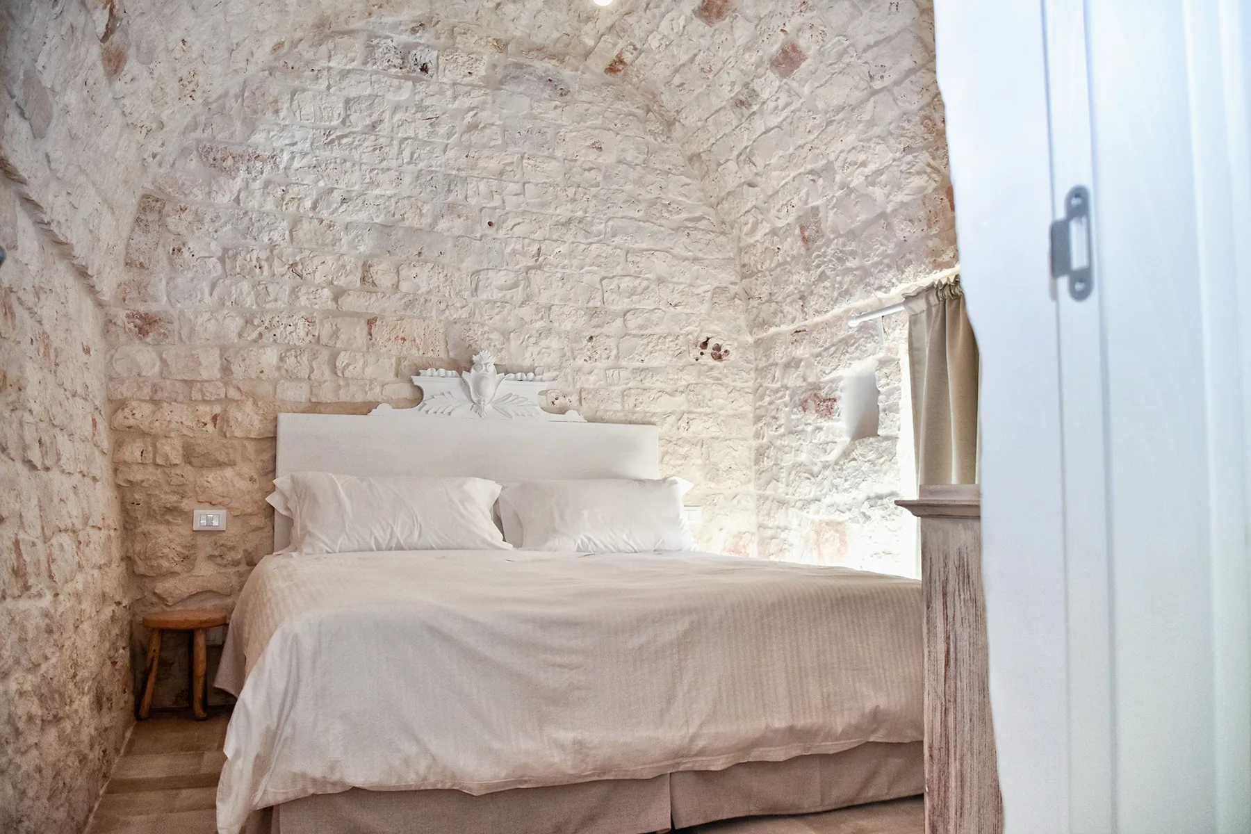 Un dormitorio con una cama frente a una pared de piedra clara.