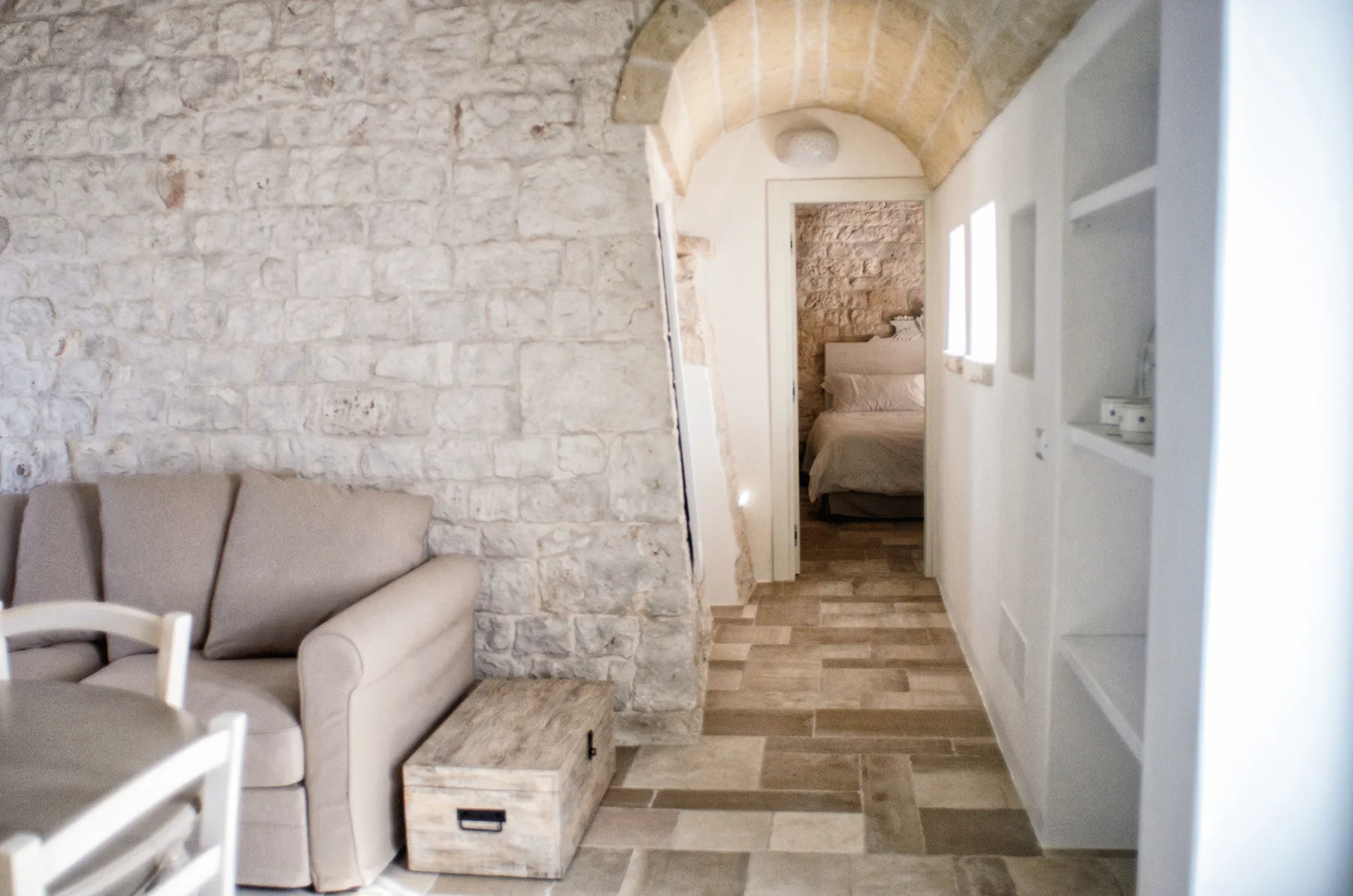 Una zona de estar con paredes de piedra da a un pasillo estrecho que conduce a un dormitorio.