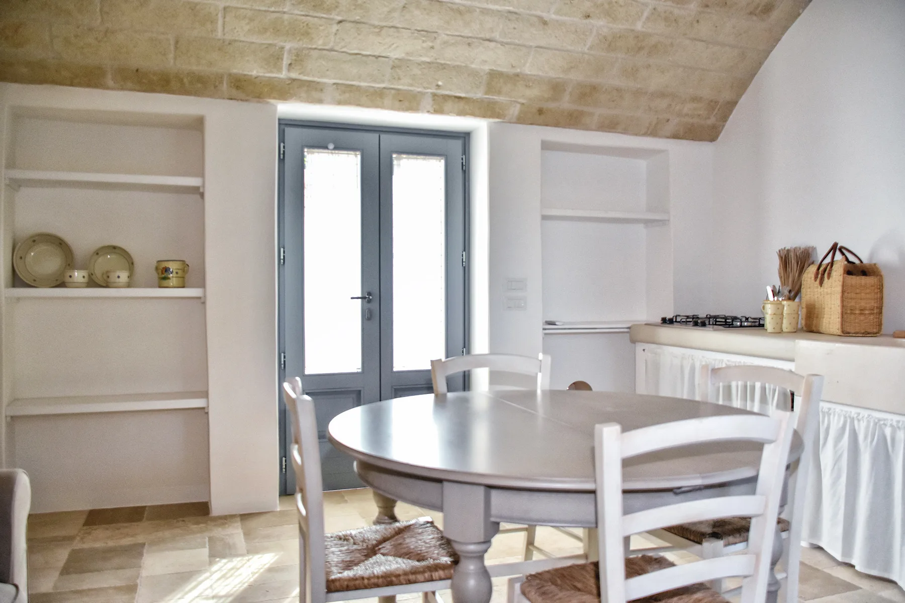 Un comedor luminoso con una mesa redonda junto a puertas de vidrio y una pequeña cocina.