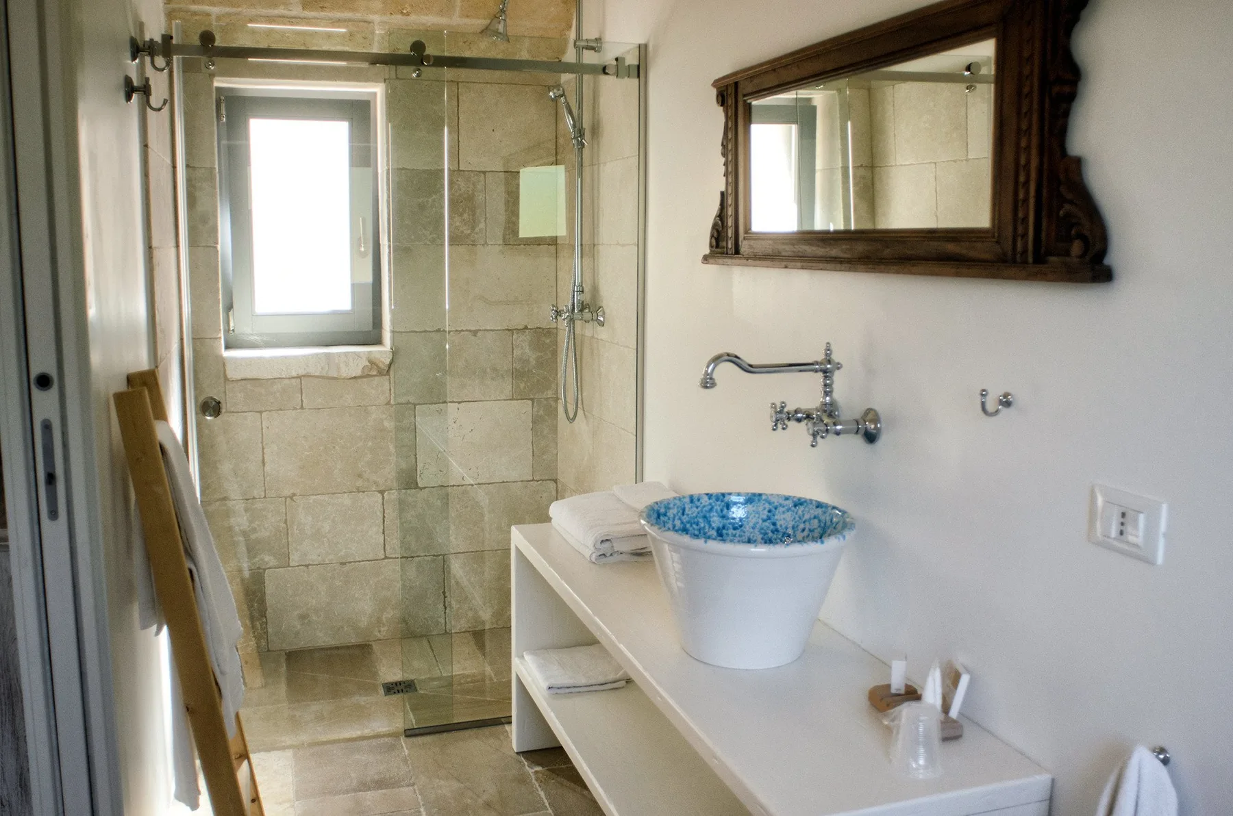 Un baño con una ducha de vidrio, un lavabo azul y un espejo de pared.