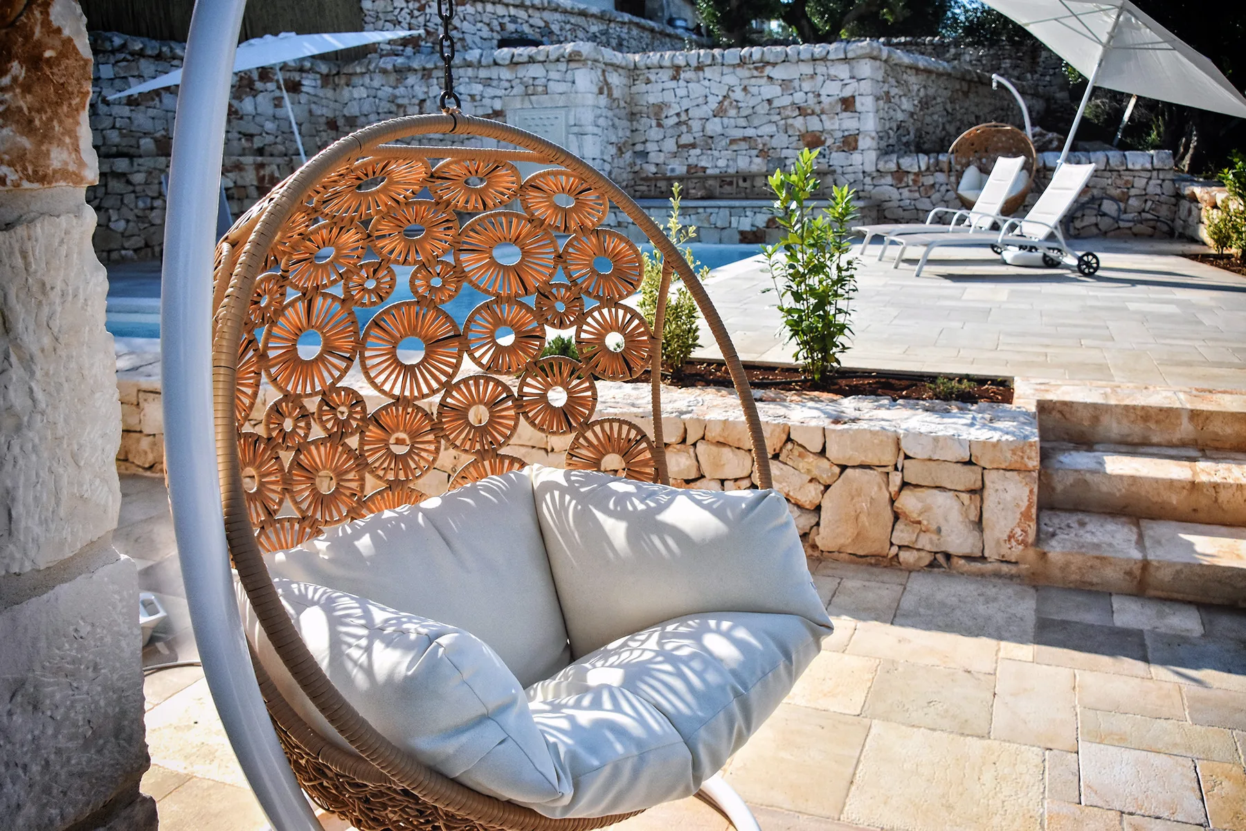 Un patio cuenta con un asiento colgante acolchado junto a una piscina soleada.