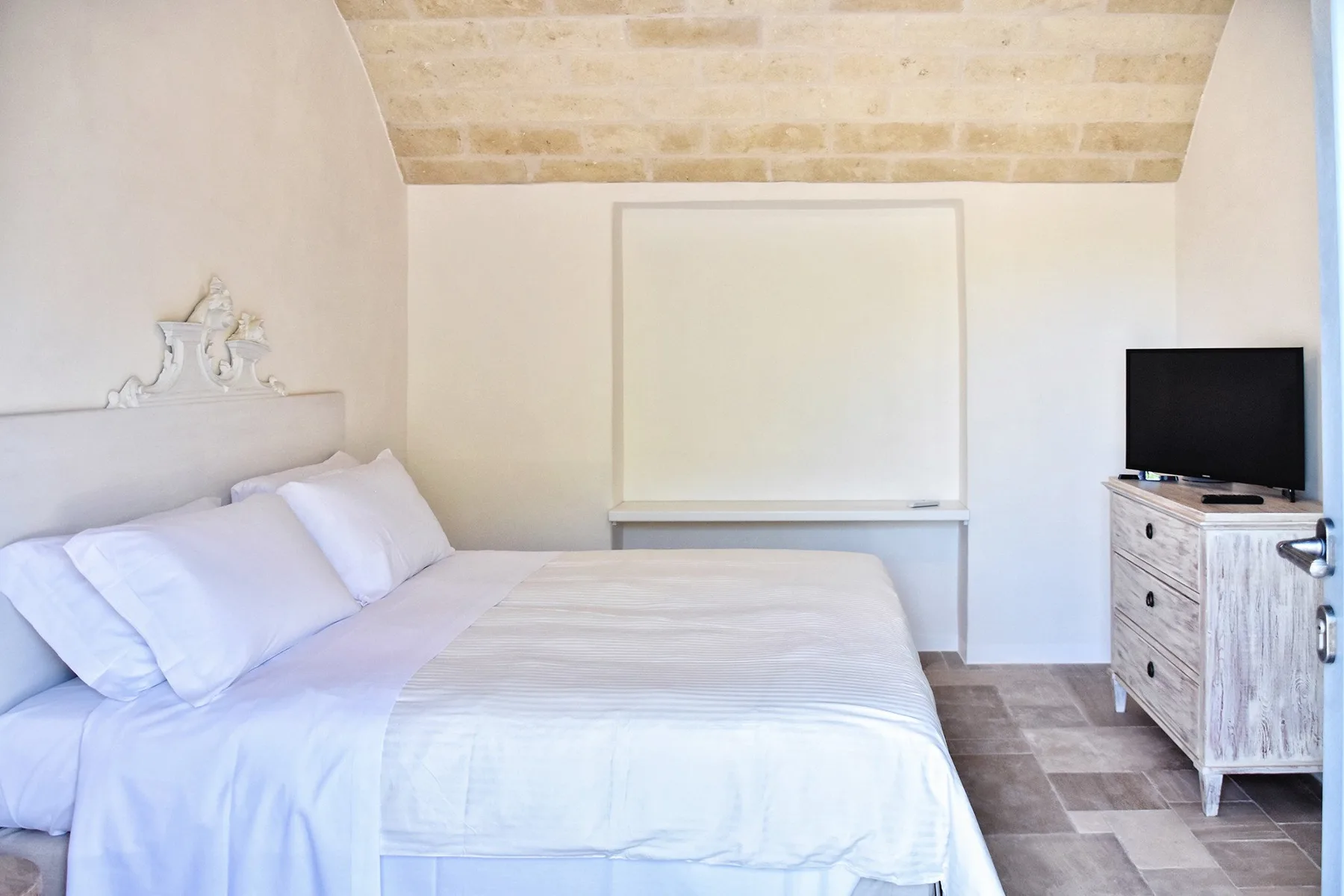 Un dormitorio luminoso con una cama bien tendida y un televisor sobre una cómoda.