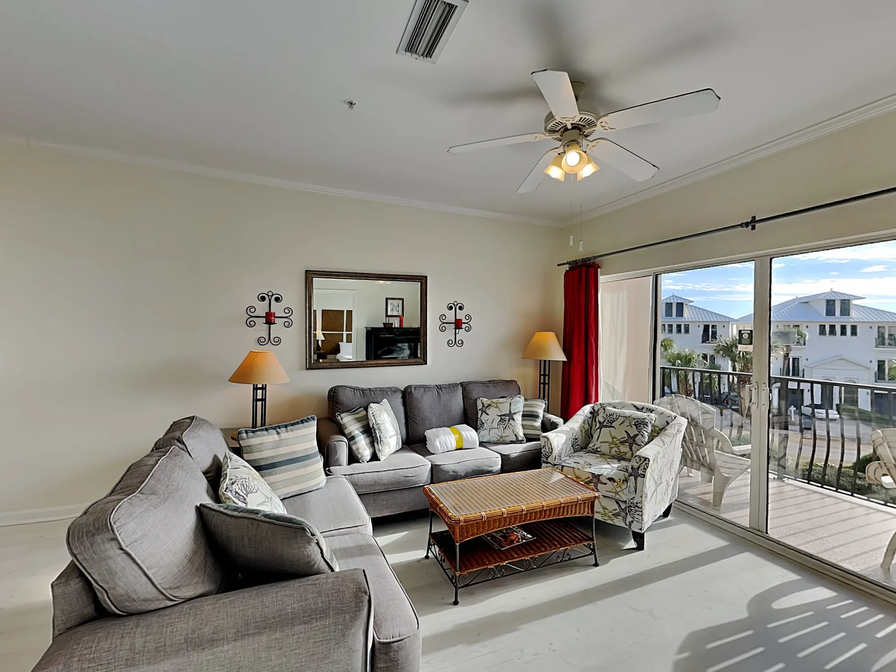 A living room with gray seating, a coffee table, and sliding glass doors opening onto a balcony.
