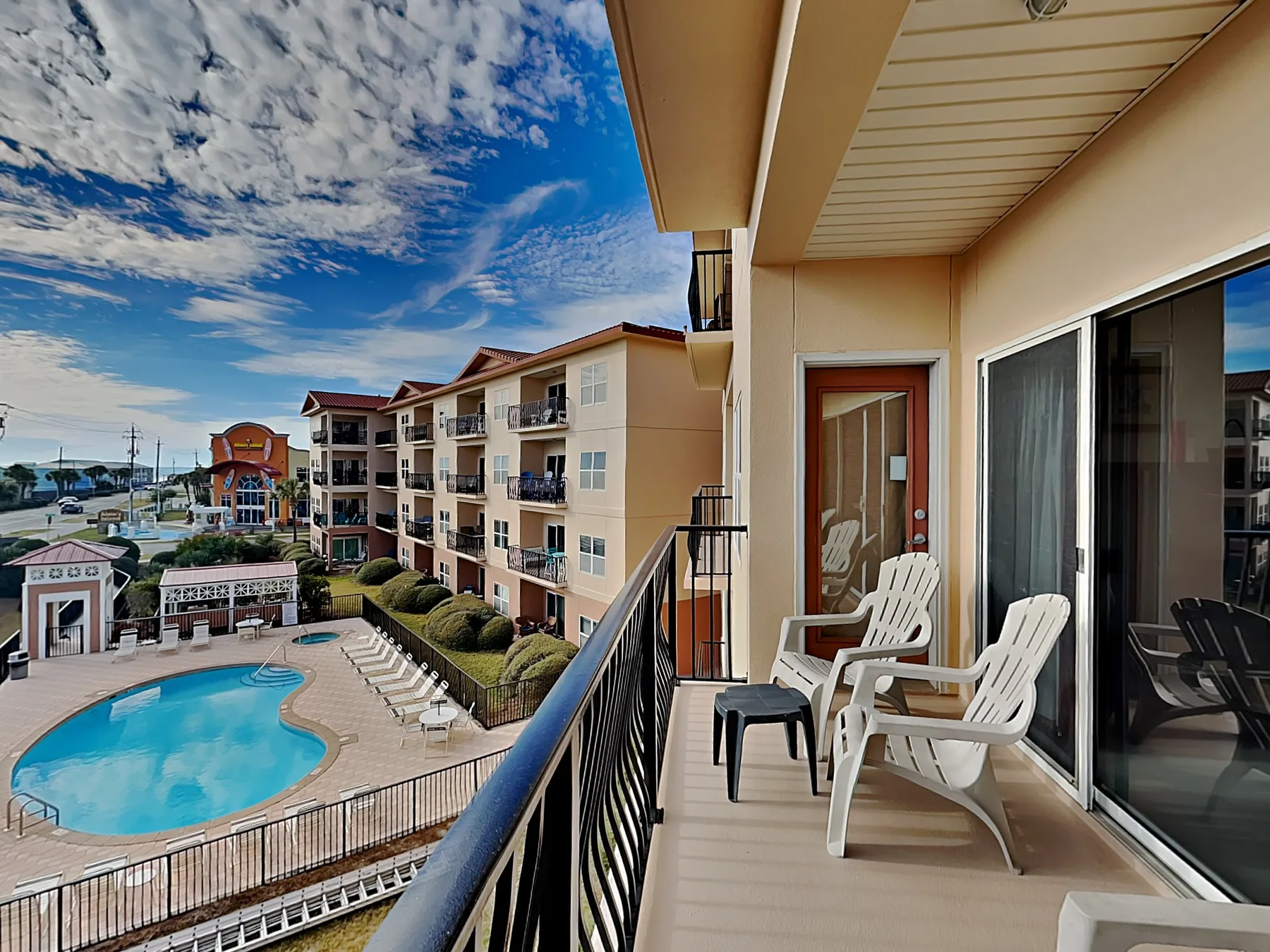 A balcony with white seating overlooks a swimming pool and nearby buildings.