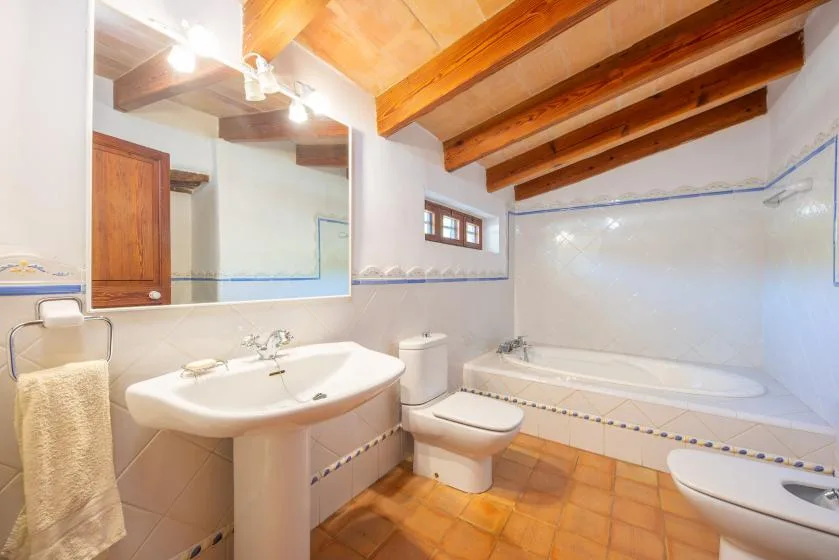 A bathroom with a sink and bathtub beneath exposed wooden ceiling beams.