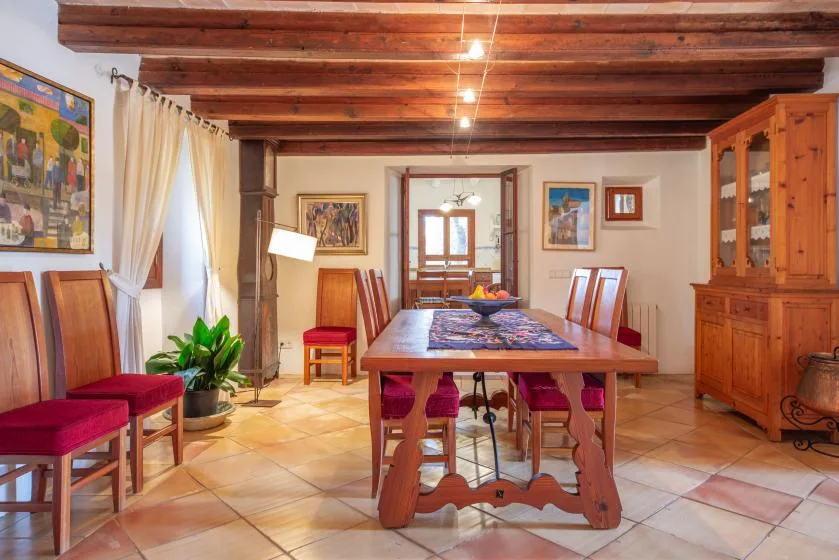 A rustic dining room with a long wooden table beneath exposed ceiling beams.