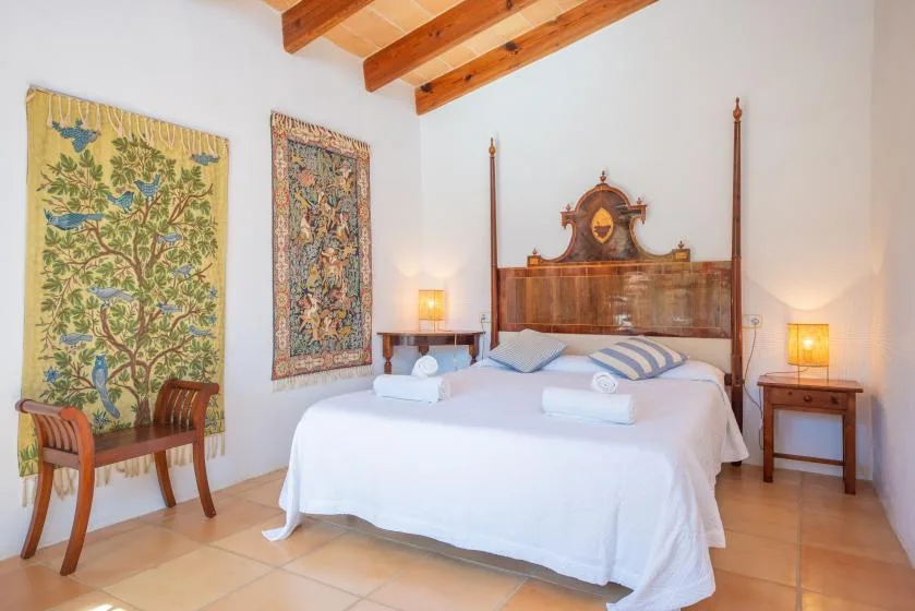 A bedroom with a large bed, bedside tables, and exposed wooden ceiling beams.