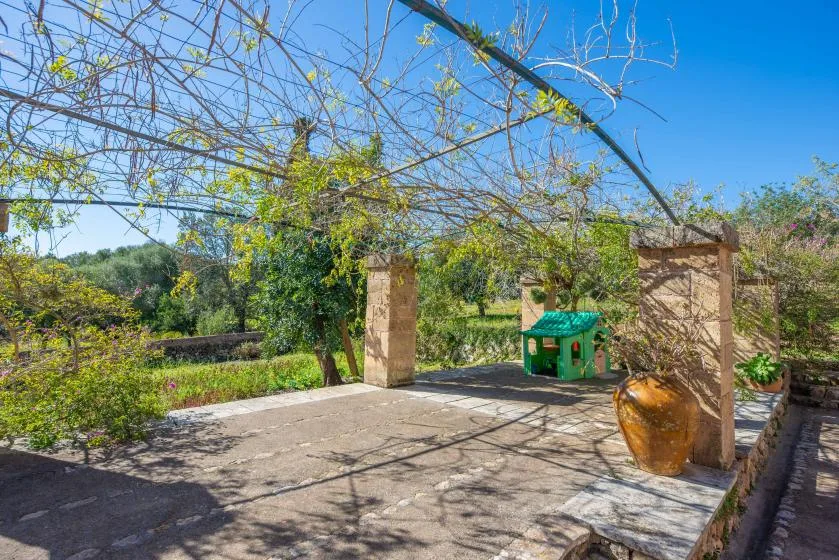 A sunlit stone patio with garden greenery and a small green play structure.