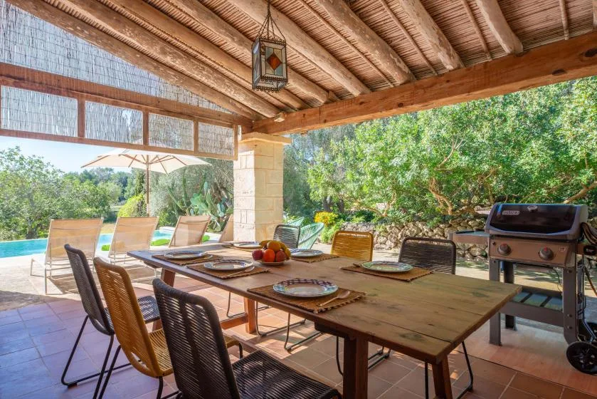A covered outdoor dining area with a wooden table beside a swimming pool.