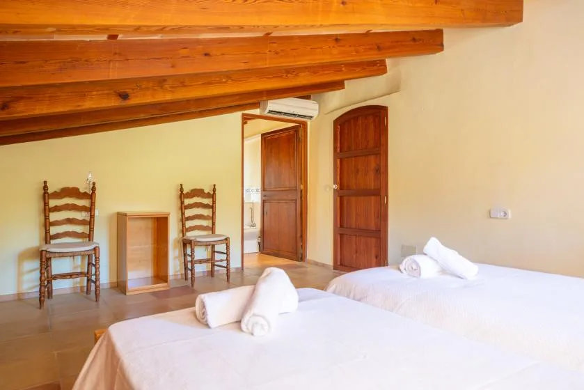 A bedroom with two beds, wooden chairs, and exposed ceiling beams.