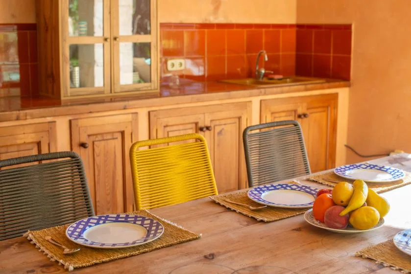 A dining table set with plates and fruit sits in front of a kitchen counter.