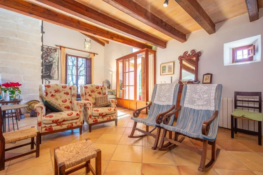 A rustic living room with floral seating and wooden ceiling beams.