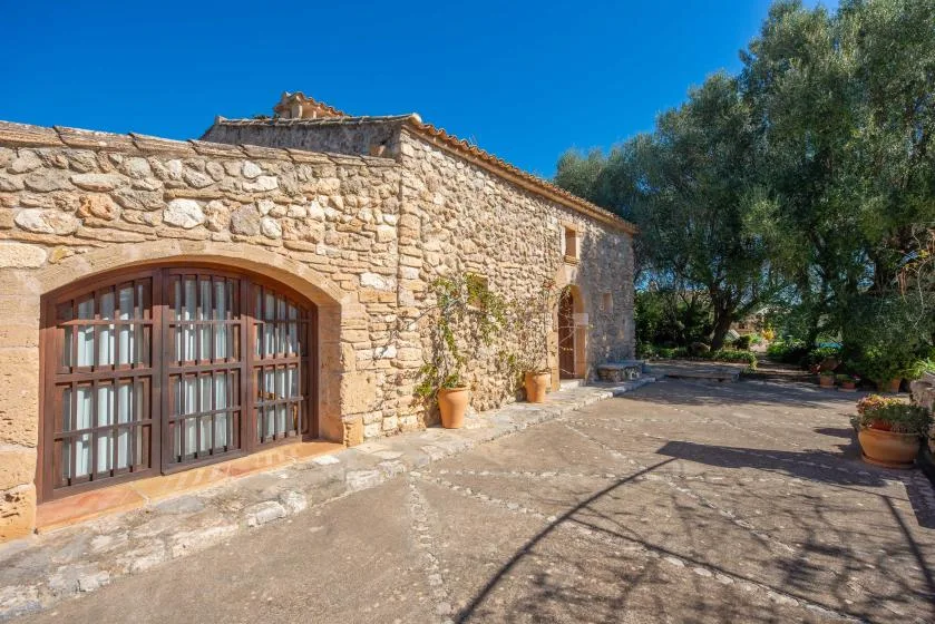 A stone building with arched wooden doors opens onto a sunny courtyard.