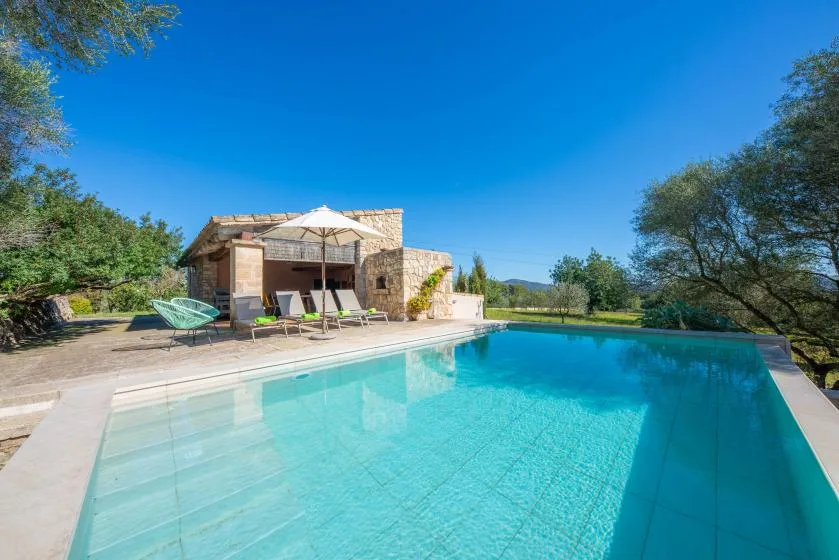 A swimming pool in front of a stone building, with outdoor seating and an umbrella.