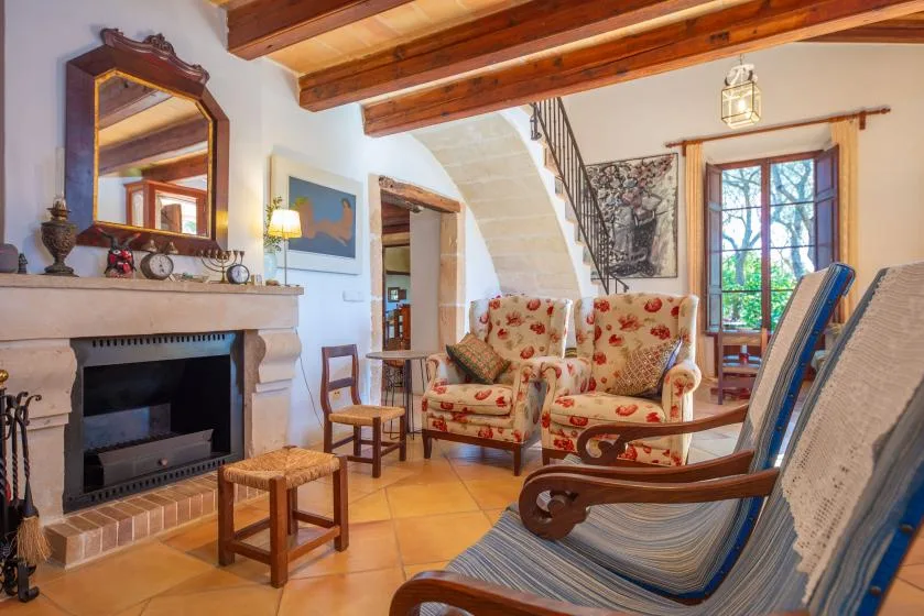 A sitting room with a fireplace, patterned armchairs, and exposed ceiling beams.