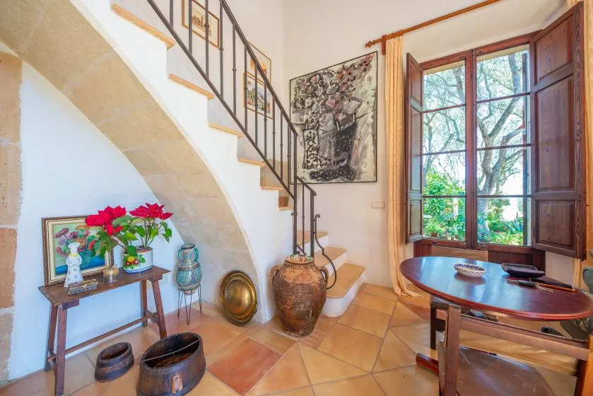 A tiled interior with a staircase, a large window, and a wooden table.