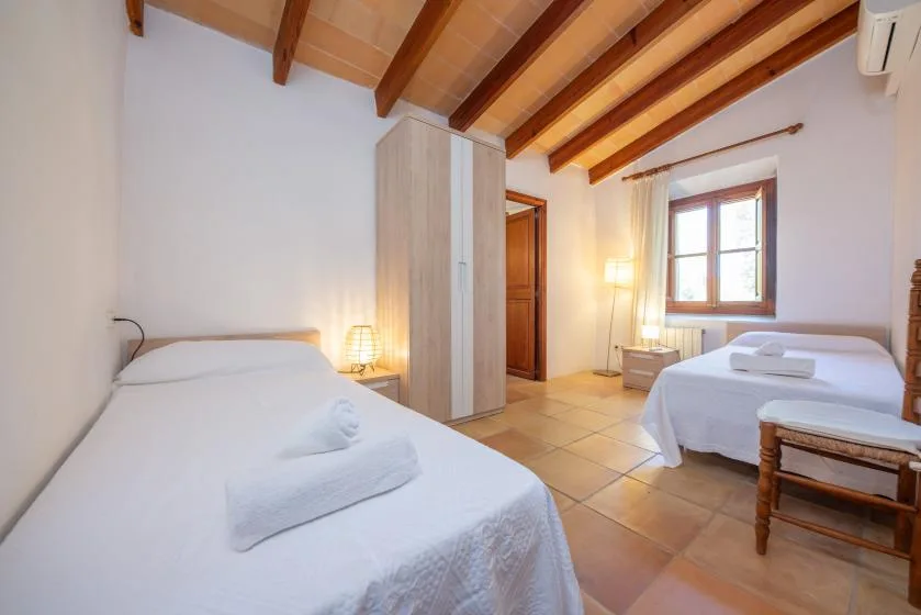 A bright bedroom with two beds, a wardrobe, and exposed wooden ceiling beams.