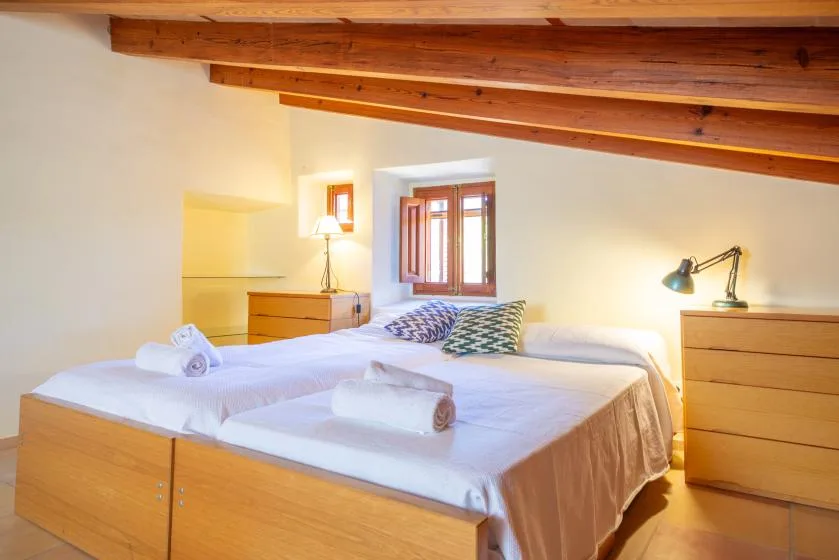 A bedroom with two beds, wooden ceiling beams, and a window.