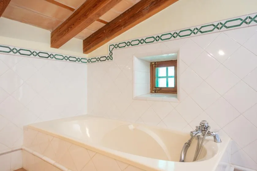 A tiled bathroom with a bathtub and a small window.