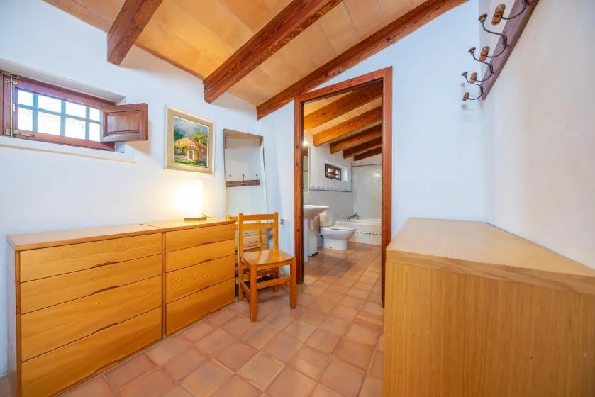 A tiled room with wooden storage, a chair, and an open doorway to a bathroom.